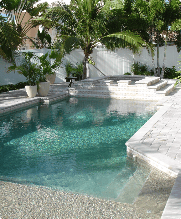 Freeform pool with a raised spa and travertine deck, enclosed by a white privacy wall and potted palms
