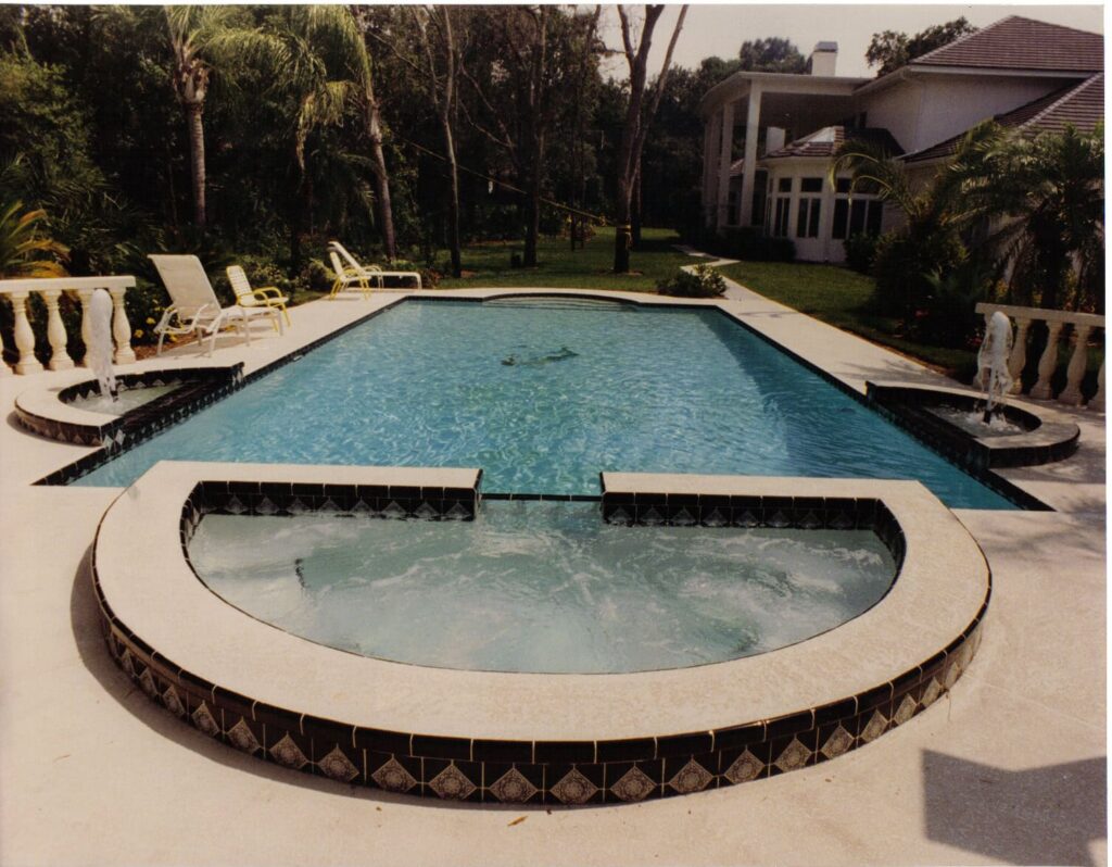 Long rectangular pool with a circular raised spa in front of a large home