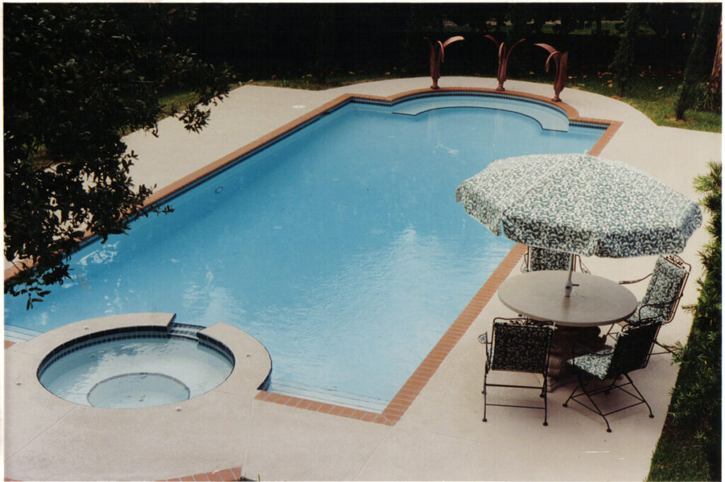 Freeform pool with an attached round spa and a patio dining set