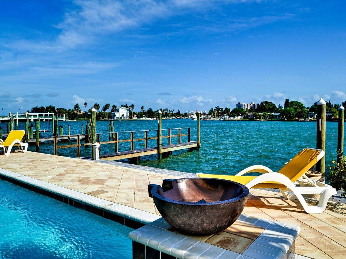 Waterfront pool deck with loungers and a fire bowl overlooking the bay